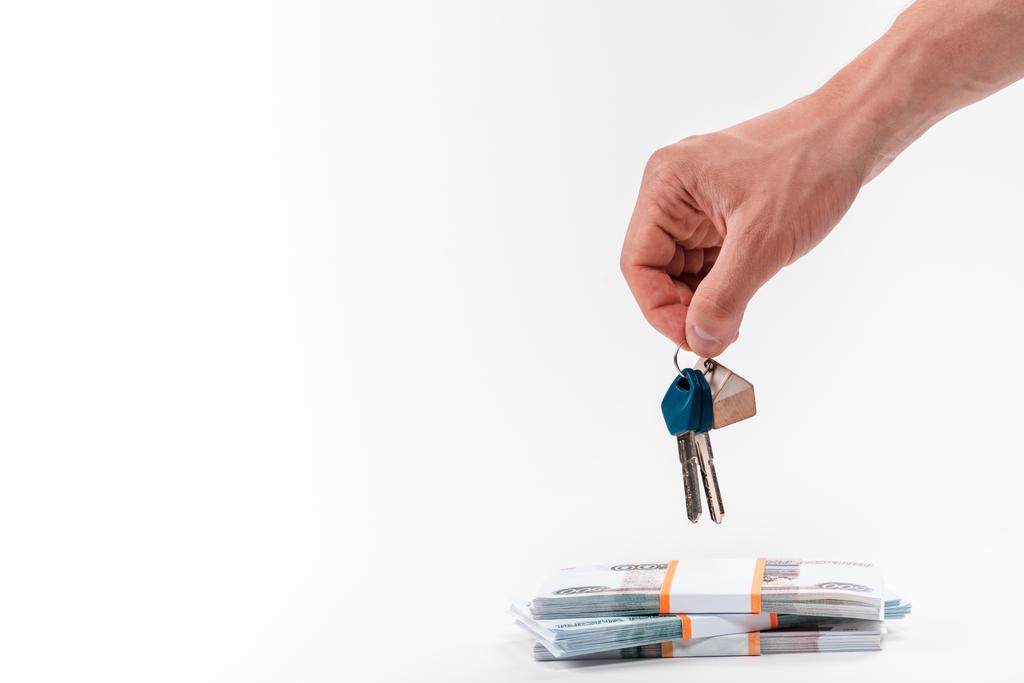 vista ritagliata di uomo in possesso di chiavi vicino pile con denaro russo isolato su bianco
   - Foto, immagini