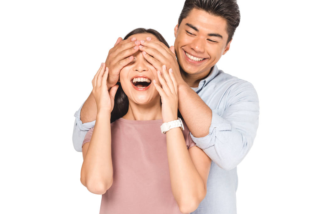 весёлый азиатский мужчина закрывает глаза улыбающейся девушки с изолированными на белом руками
 - Фото, изображение