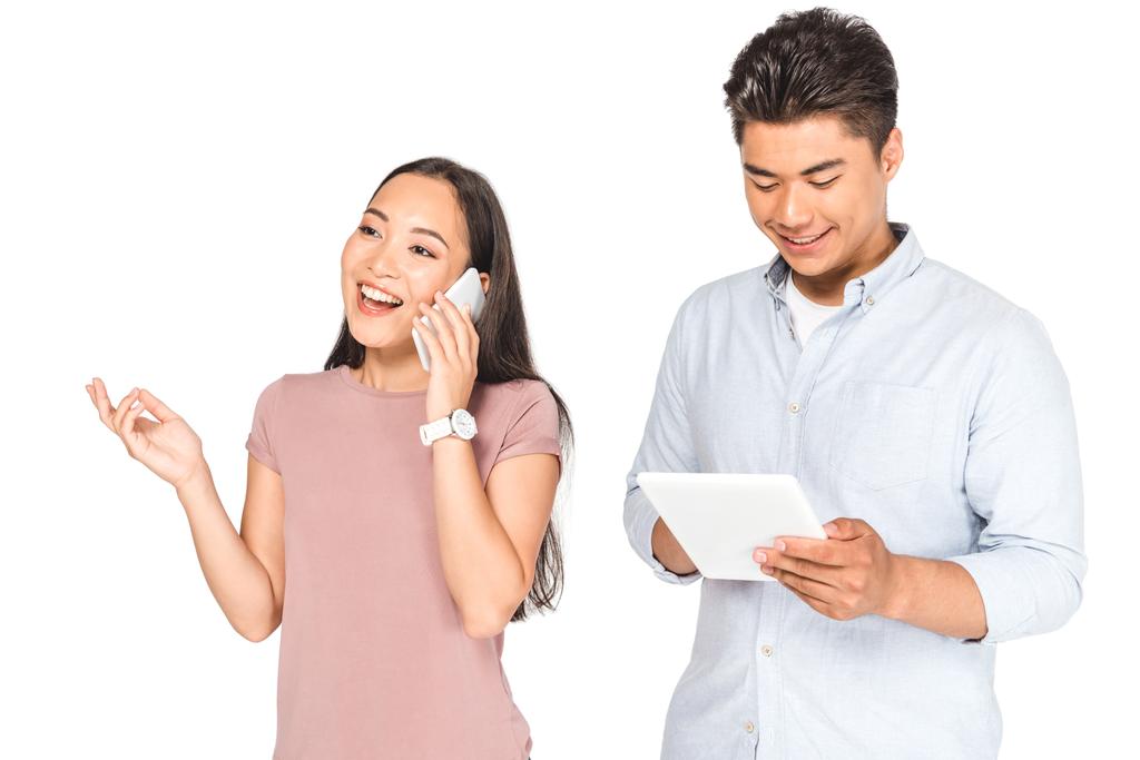 白で隔離されたラップトップを使用してボーイフレンドの近くでスマートフォンで話す陽気なアジアの女性 - 写真・画像