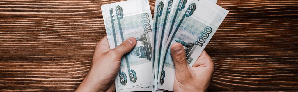 panoramic shot of man holding russian money near table  - Фото, зображення