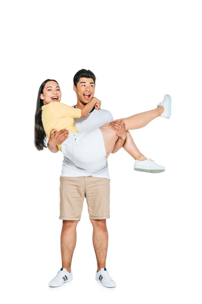schöner asiatischer Mann hält lächelnde Freundin auf Händen auf weißem Hintergrund - Foto, Bild