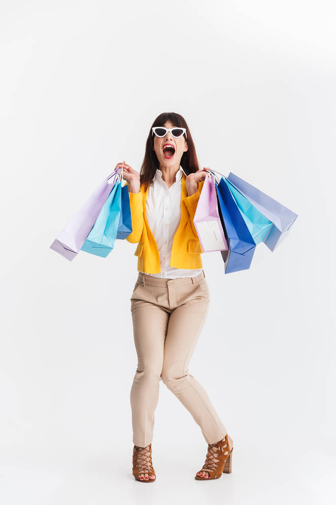 Impresionada joven mujer de negocios posando aislada sobre fondo blanco sosteniendo bolsas de compras
. - Foto, imagen