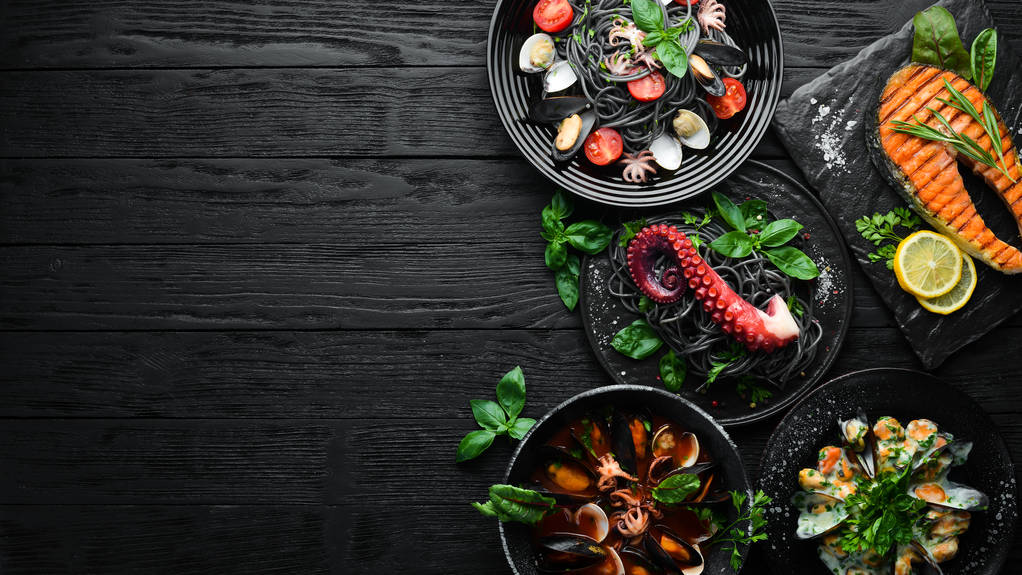 Reihe von Meeresfrüchten. Meeresfrüchte auf einem Teller. auf schwarzem Holzgrund. Ansicht von oben. freier Kopierraum. - Foto, Bild