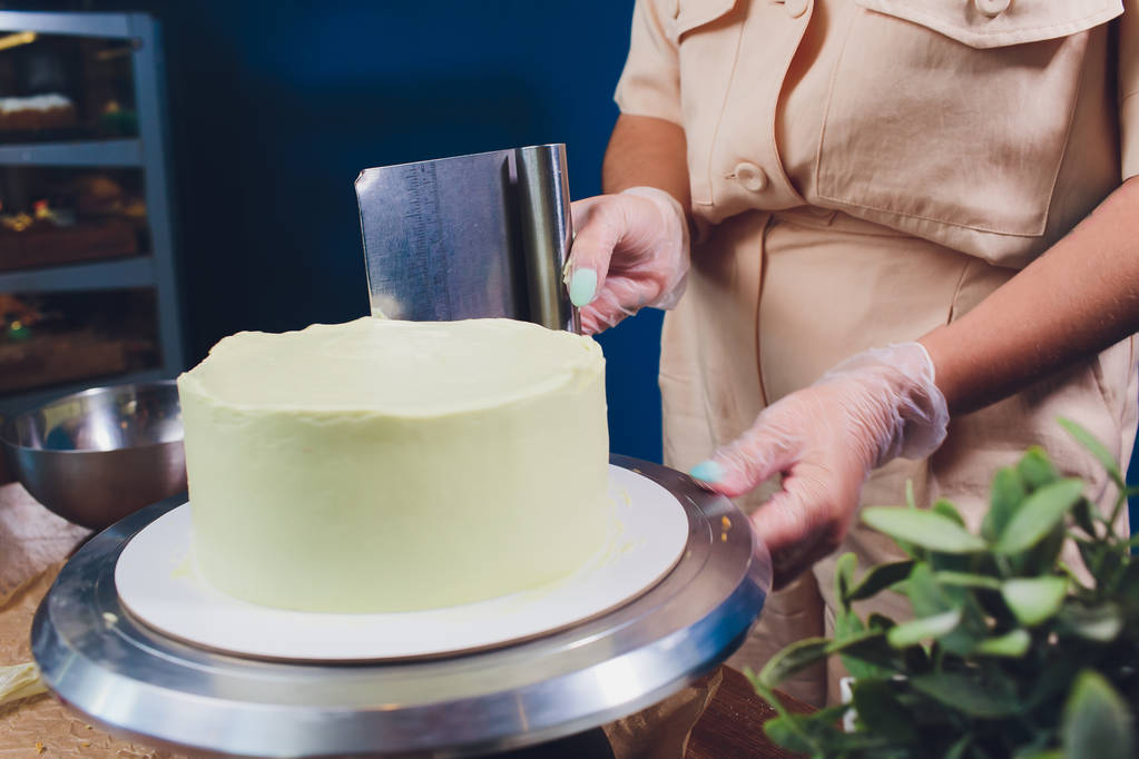 Frauenhände backen Kekskuchen mit weißer Sahne mit einem Kochspachtel. - Foto, Bild
