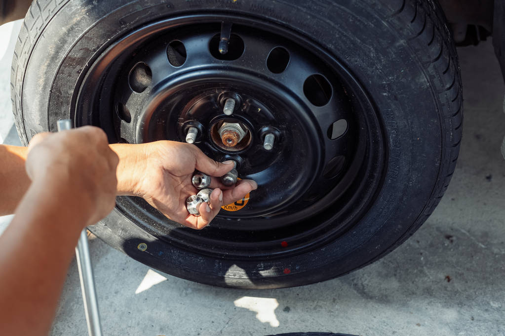 Les mains du mécanicien ramassent l'écrou de la roue de la voiture.Changez un pneu de voiture à plat au parking avec entretien des pneus, pneu de voiture endommagé
. - Photo, image