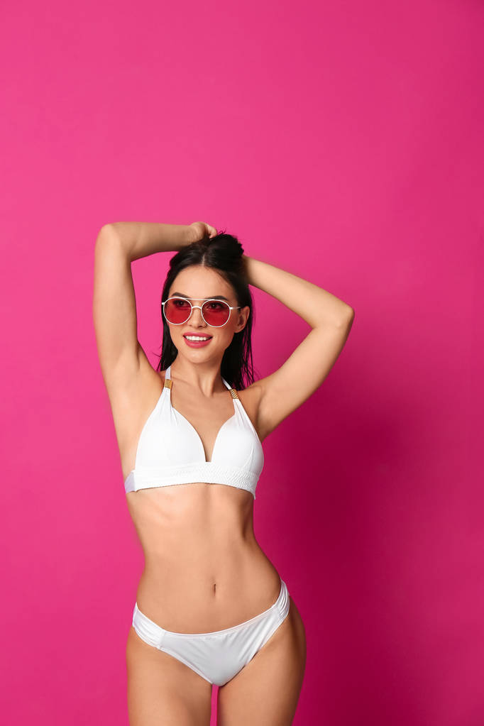Mooie jonge vrouw in witte bikini met zonnebril op roze achtergrond - Foto, afbeelding