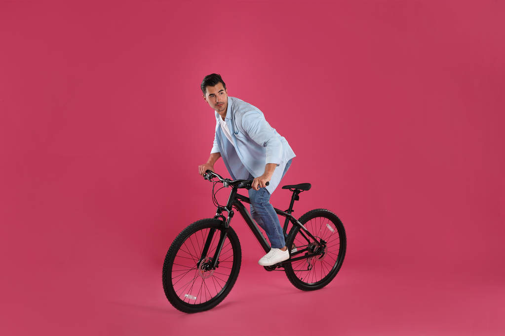 Όμορφος νέος άντρας με μοντέρνο ποδήλατο σε ροζ φόντο - Φωτογραφία, εικόνα