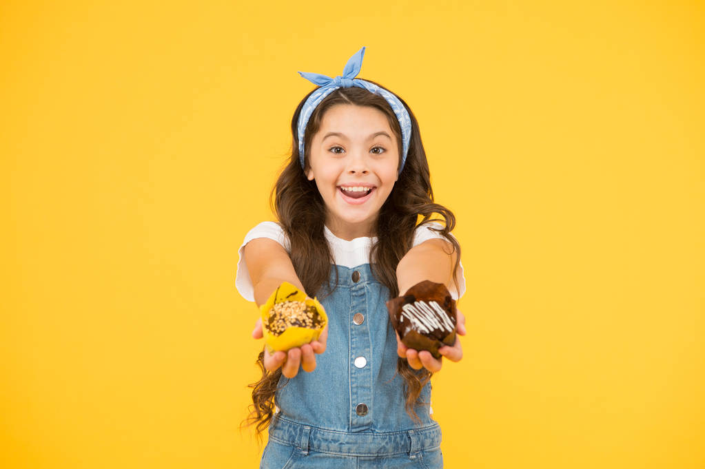 Kenyér és cukrász koncepció. Gyerek lány tartsa mázas muffin. Finom cupcakes. Boldog gyermekkorban. Imádnivaló mosolygó gyermek Cupcakes sárga háttér. Cafe étterem étel. Fincsi cupcakes - Fotó, kép