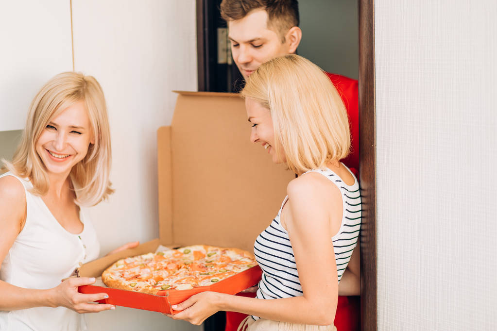Дві молоді білошкірі жінки отримують піцу з доставки чоловіка вдома
 - Фото, зображення