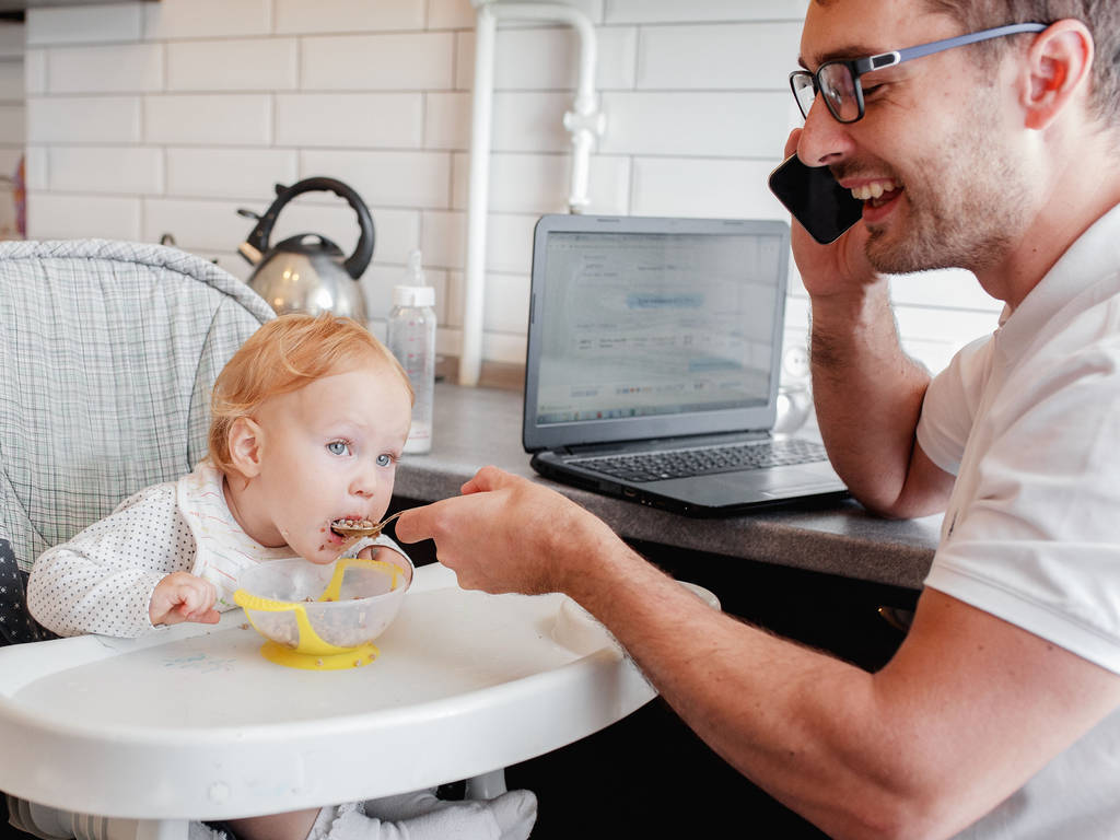 glücklicher junger Vater, der zu Hause arbeitet und mit einem kleinen Mädchen sitzt. - Foto, Bild