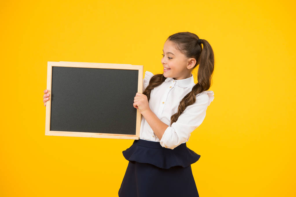 Kleines Mädchen, großer Traum. kleines Kind mit schwarzer Tafel für Schulwerbung auf gelbem Hintergrund. Kleines Kind mit leerer Kreidetafel für Ihren Text. kleines Schulmädchen hält Tafel, Kopierraum - Foto, Bild