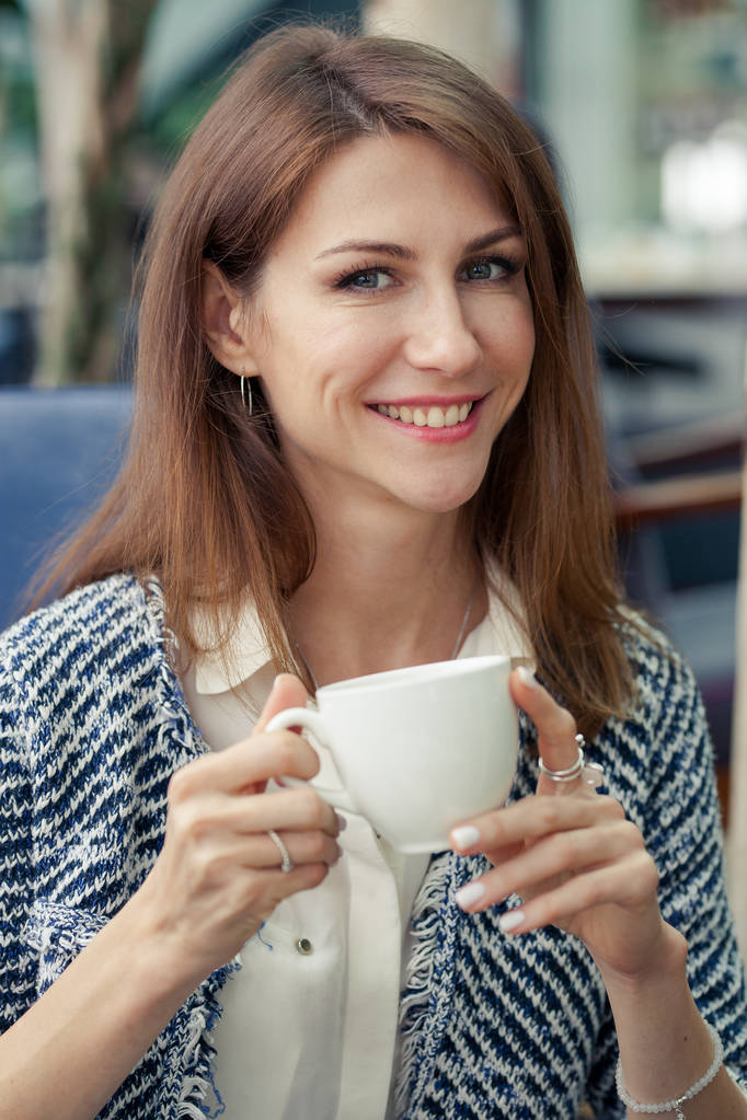 портрет привлекательной улыбающейся брюнетки молодой деловой женщины. Девушка держит в руках белую чашку и смотрит вдаль
 - Фото, изображение
