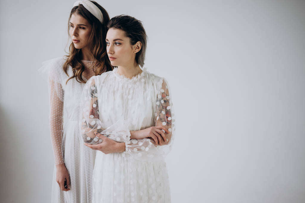 twee modellen dragen witte jurken poseren op lichte achtergrond, Studio schot  - Foto, afbeelding