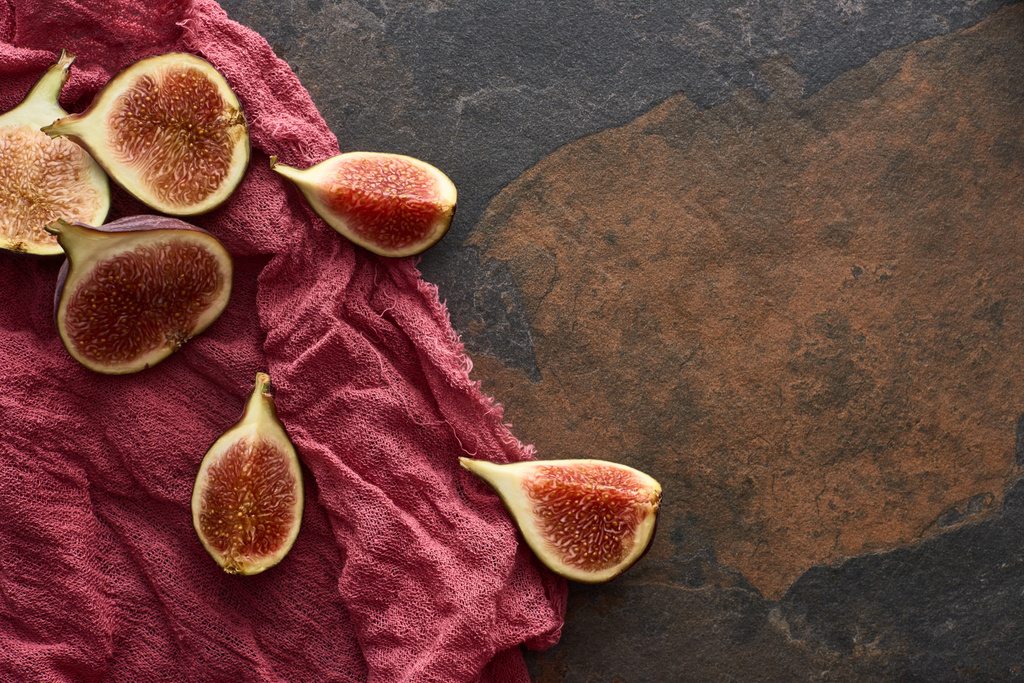 top view of ripe cut delicious figs on rustic red cloth on stone background - Photo, Image