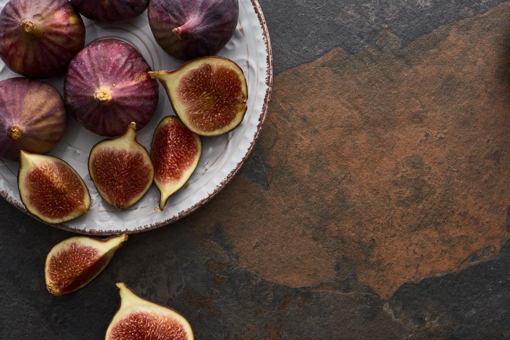 top view of ripe whole and cut delicious figs on plate on stone background - Photo, Image