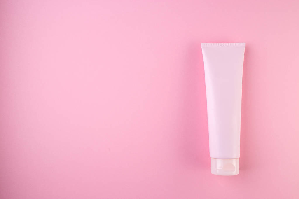 Tubo de plástico com rosto ou creme corporal em fundo rosa pastel
  - Foto, Imagem