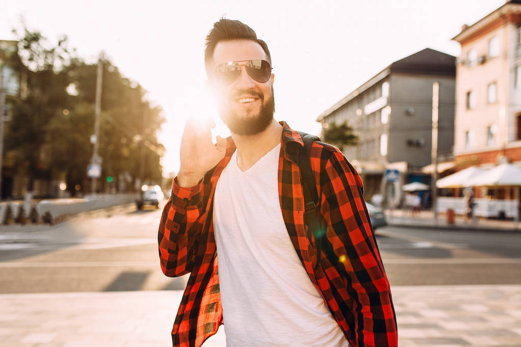 Elegante tipo con barba en auriculares inalámbricos pasea por la ciudad y escucha música
 - Foto, Imagen
