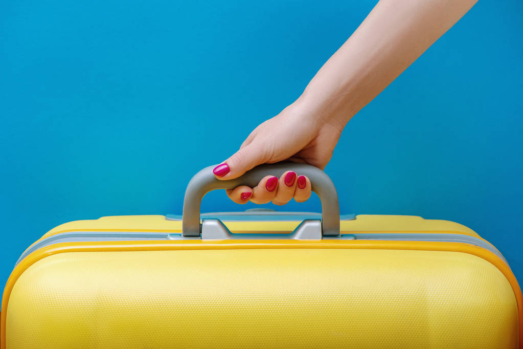 Vrouw met gele koffer in de hand op blauwe achtergrond. - Foto, afbeelding