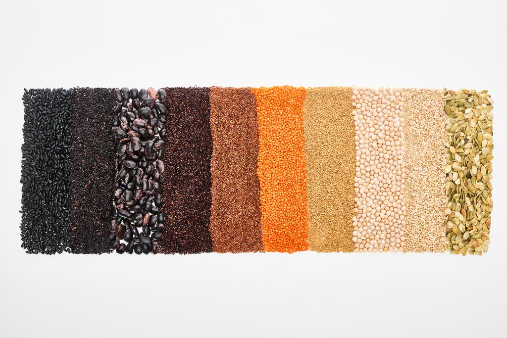 Blick von oben auf schwarze Bohnen, Reis, Quinoa, Kichererbsen, Kürbiskerne, Buchweizen und rote Linsen isoliert auf weiß - Foto, Bild