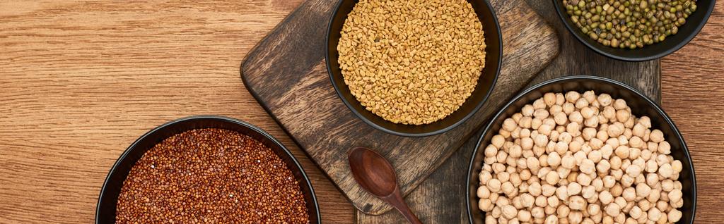 panoramic shot of bowls with roasted buckwheat, chickpea and beans near wooden spoon on wooden cutting boards - Photo, Image