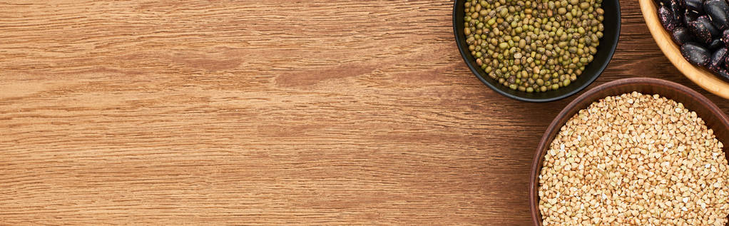 tiro panorâmico de tigelas com trigo sarraceno cru e feijão moong verde na superfície de madeira
 - Foto, Imagem