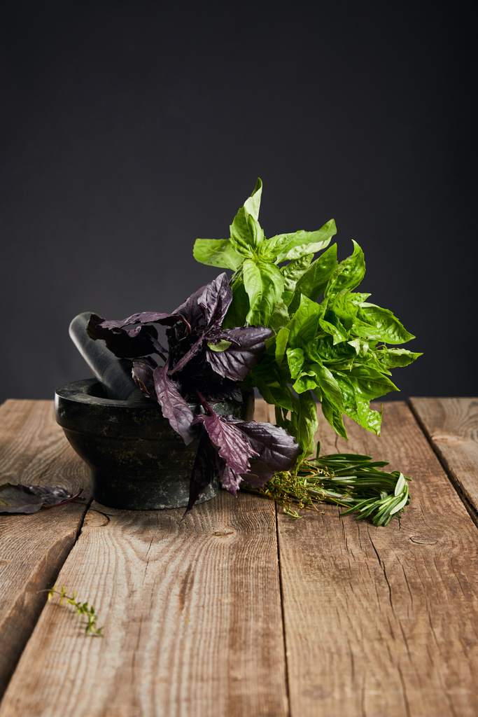 mortar with fresh green and purple basil with rosemary on wooden table isolated on black - Photo, Image
