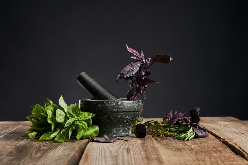 黒で隔離された木製のテーブルの上に新鮮な緑と紫のバジルの近くに害虫を持つモルタル - 写真・画像