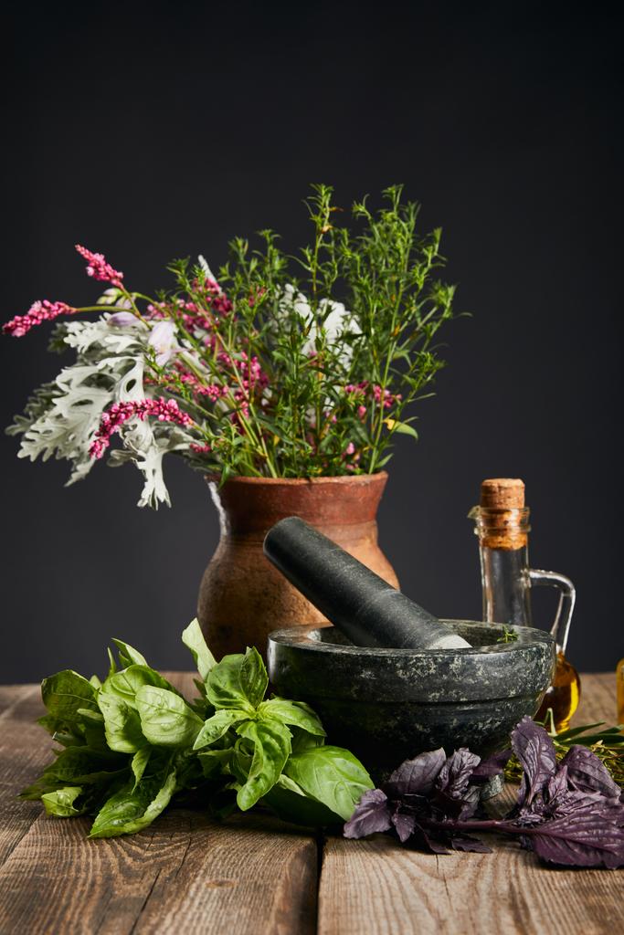 сірий розчин, глиняна ваза з травами і пляшка на дерев'яному столі ізольовані на чорному
 - Фото, зображення