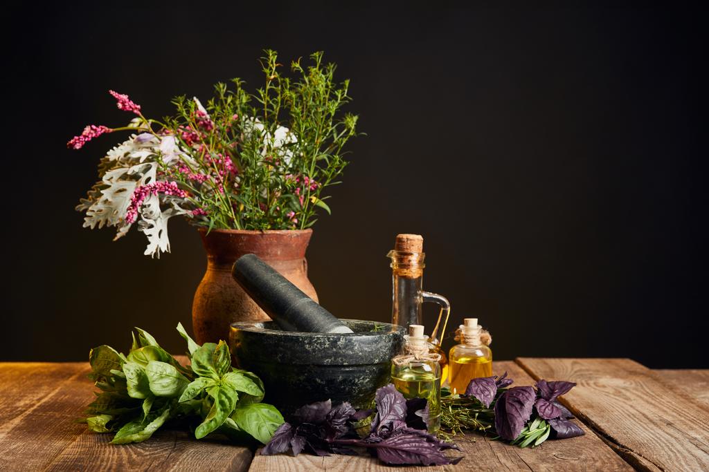 szary zaprawy w pobliżu gliny wazon ze świeżych kwiatów i ziół na drewnianym stole izolowane na czarno - Zdjęcie, obraz