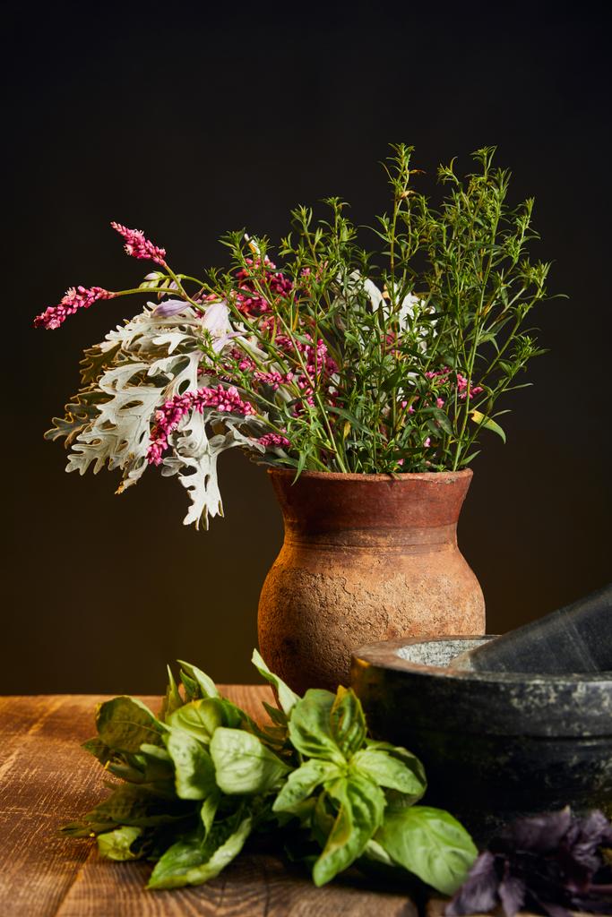 jarrón de arcilla con flores silvestres frescas y hierbas en la mesa de madera aislada en negro
 - Foto, Imagen