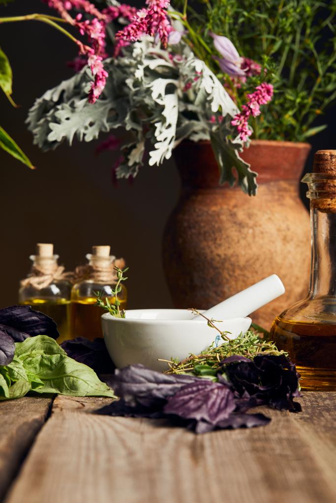 malta con pestello vicino bottiglie con olio e vaso con fiori freschi su superficie di legno isolato su nero
 - Foto, immagini