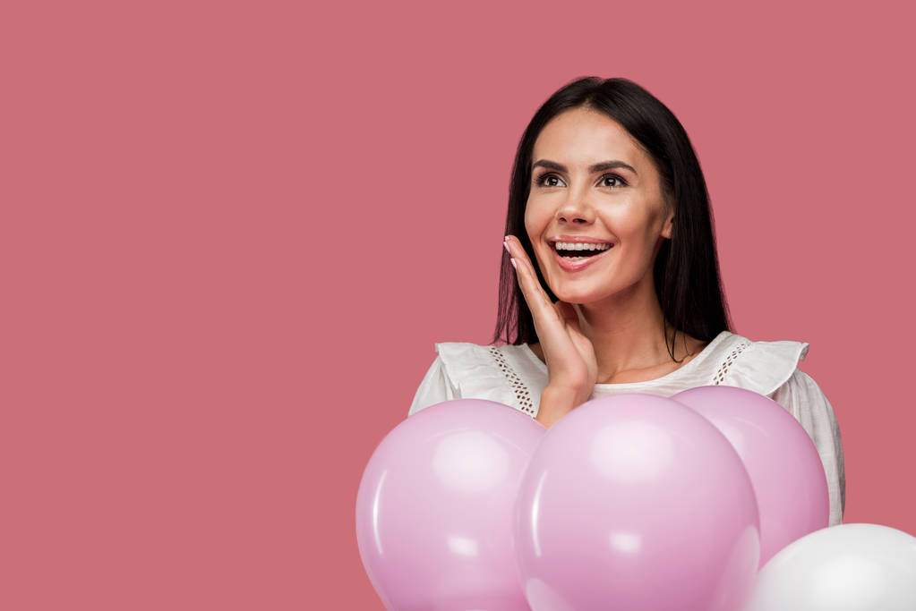 χαρούμενο κορίτσι σε φόρεμα κρατώντας μπαλόνια και συγκινητικό πρόσωπο απομονώνεται σε ροζ  - Φωτογραφία, εικόνα