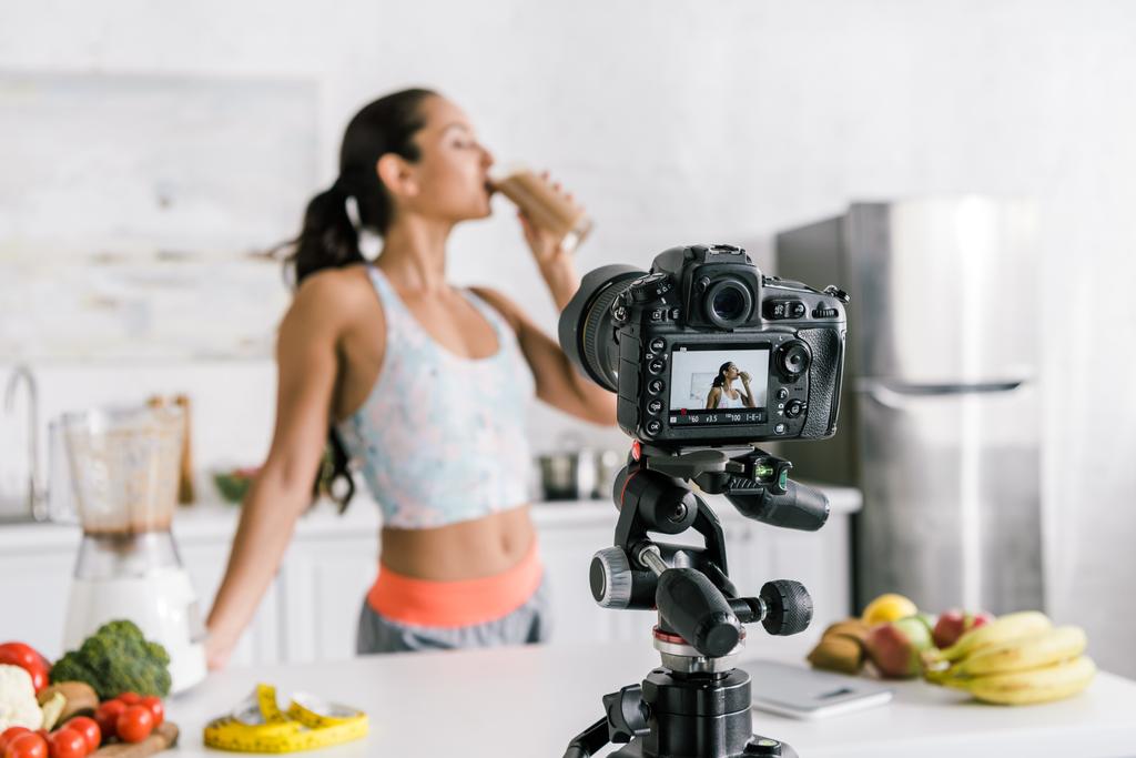 enfoque selectivo de la cámara digital con chica bebiendo batido cerca de frutas y verduras en la pantalla
 - Foto, Imagen
