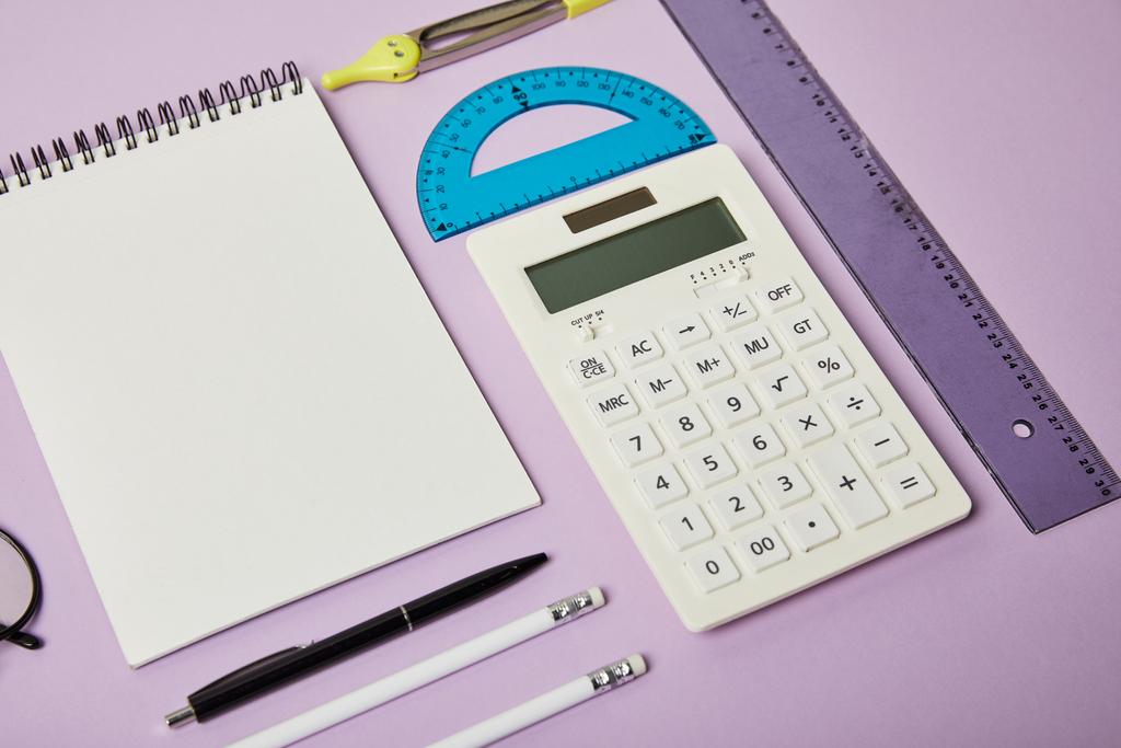righelli e calcolatrice vicino notebook e matite con penna isolata su viola
  - Foto, immagini
