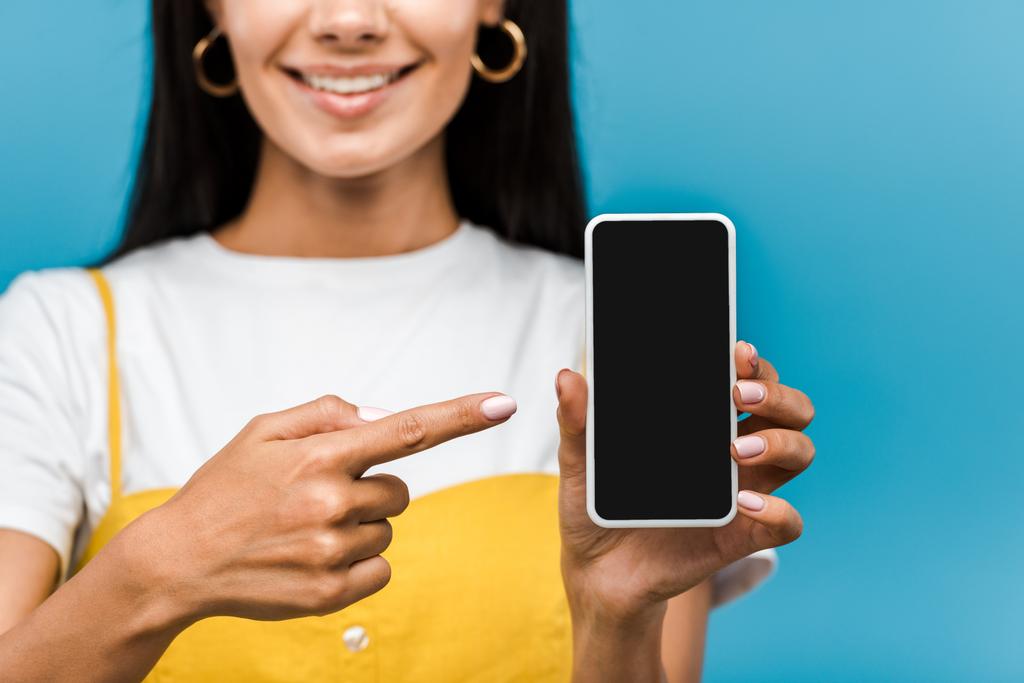 vista ritagliata della ragazza che punta con il dito allo smartphone con schermo vuoto isolato sul blu
  - Foto, immagini