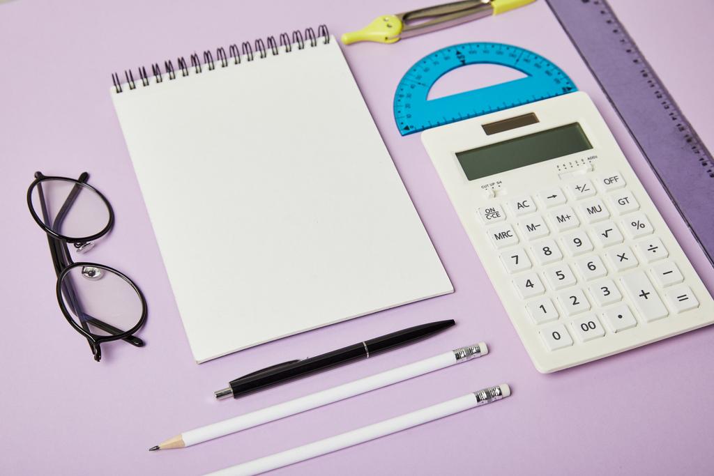 reglas y calculadora cerca de notebook y gafas aisladas en púrpura
  - Foto, imagen