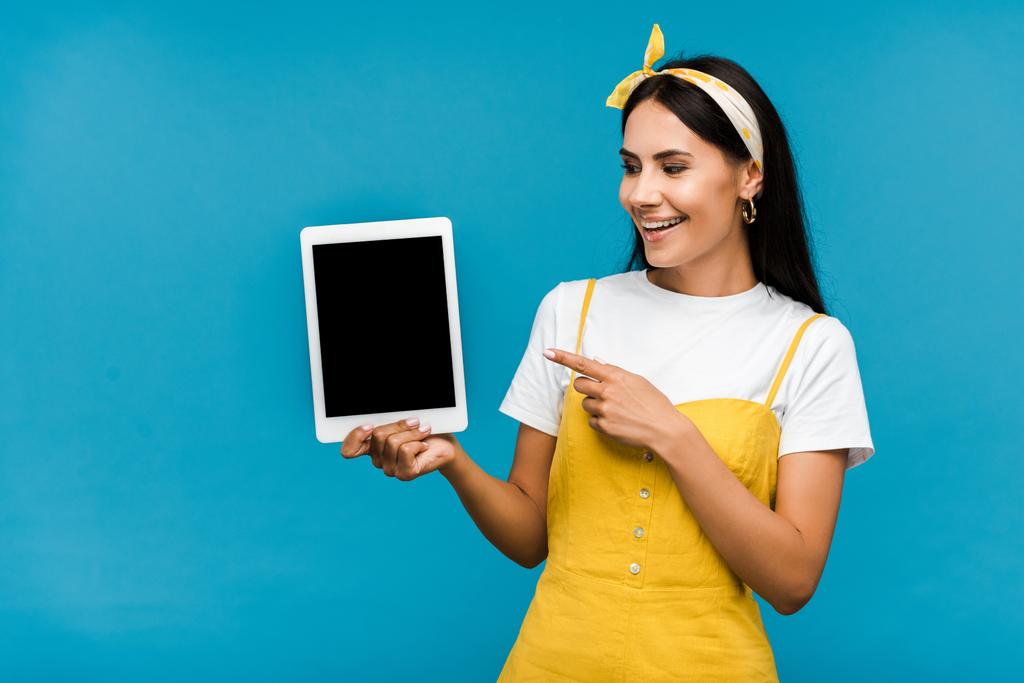 glückliches Mädchen zeigt mit dem Finger auf digitales Tablet mit leerem Bildschirm isoliert auf blau  - Foto, Bild
