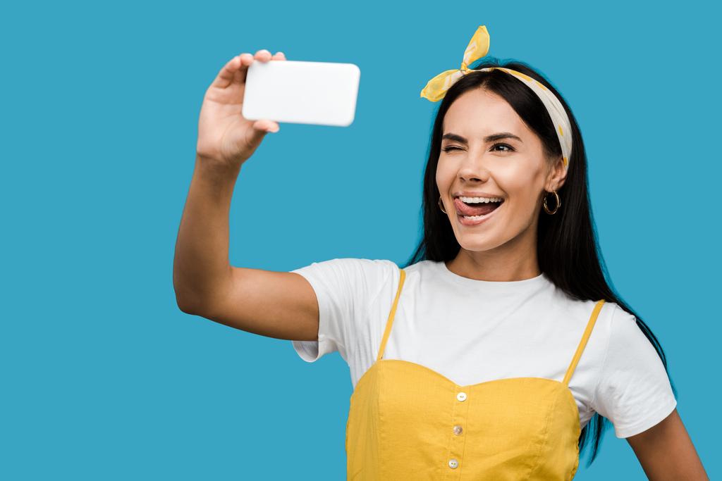 Nuori nainen ottaa selfie älypuhelimeen samalla kun näytetään kielen eristetty sininen
   - Valokuva, kuva