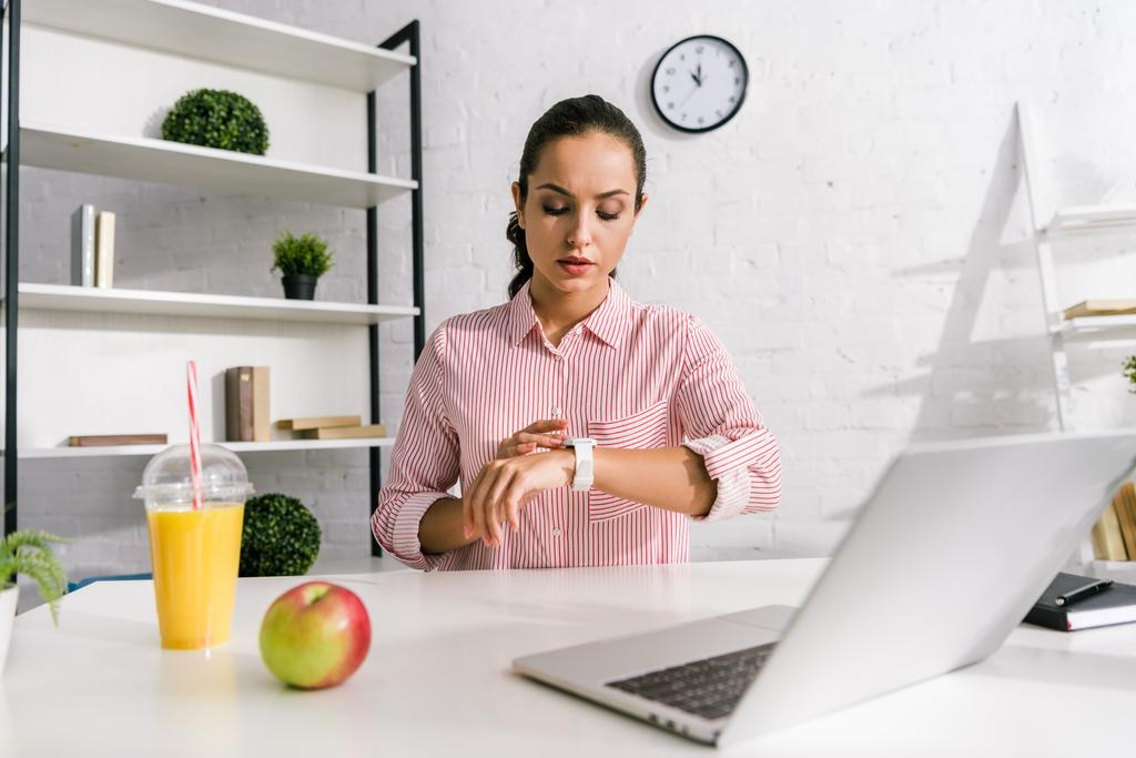 attraente ragazza guardando orologio vicino laptop e mela
  - Foto, immagini