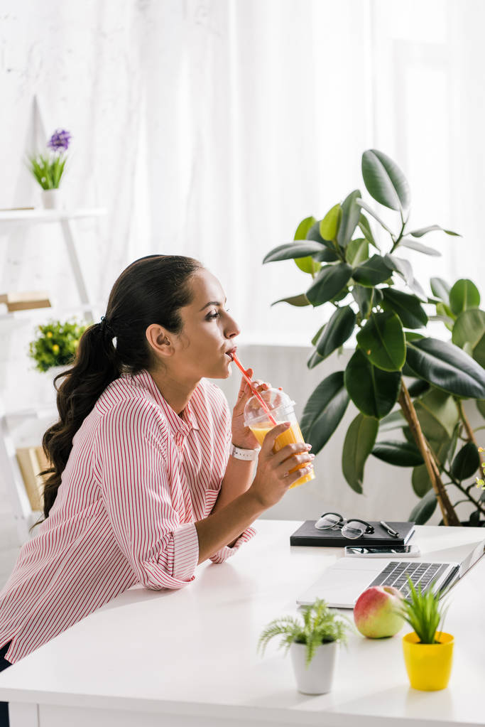 menina atraente beber suco de laranja perto do laptop
  - Foto, Imagem
