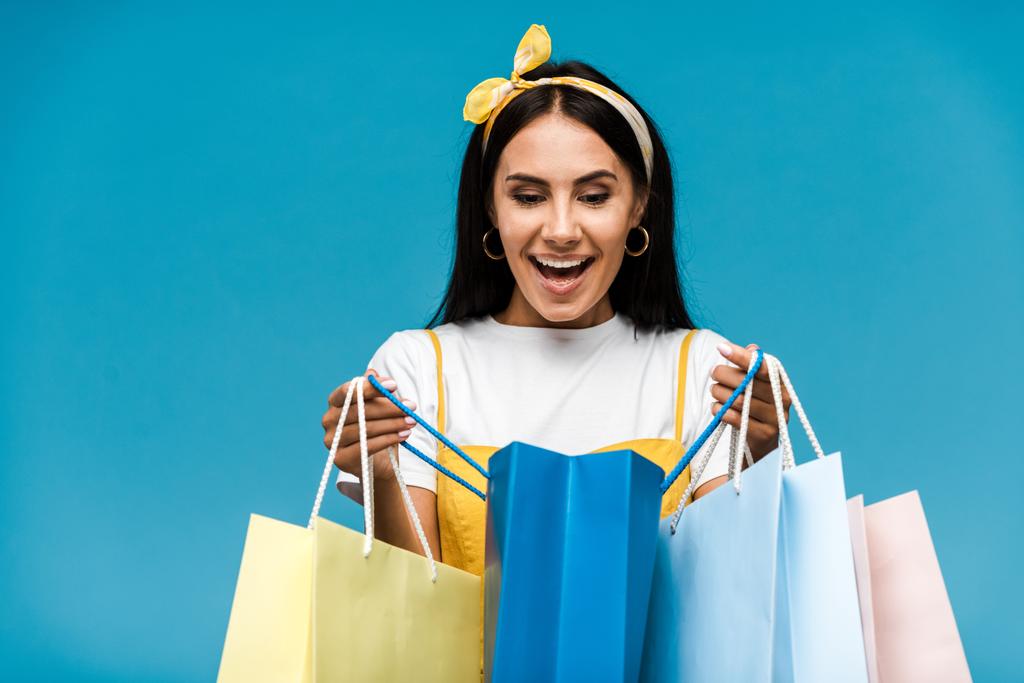 glückliche junge Frau blickt vereinzelt auf blaue Einkaufstüten  - Foto, Bild