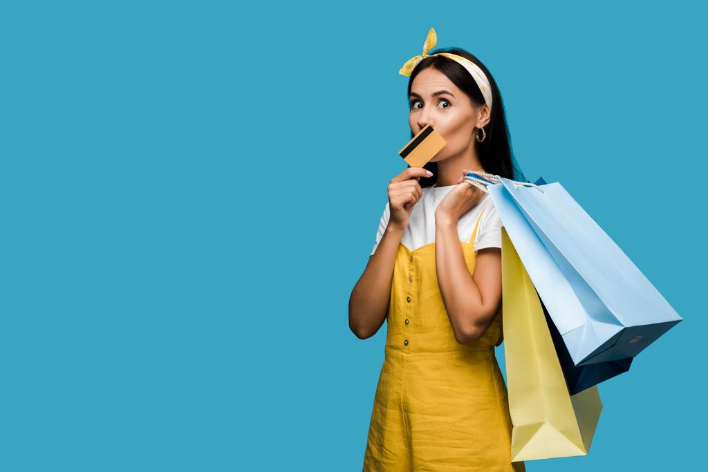 mladá žena držící kreditní kartu a nákupní tašky izolované na modré  - Fotografie, Obrázek