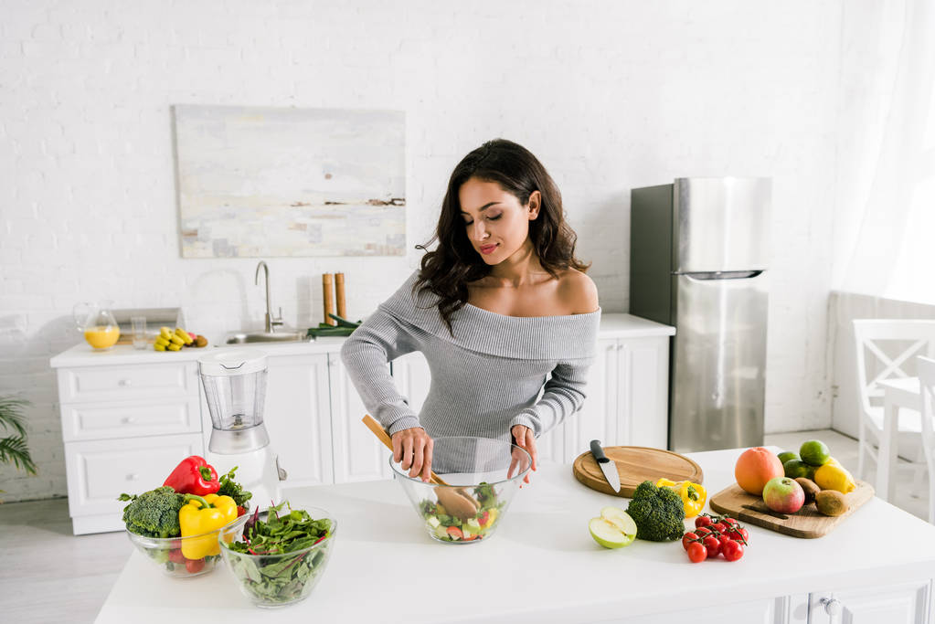 houkutteleva tyttö seisoo lähellä kulhoja salaattia ja vihanneksia
  - Valokuva, kuva