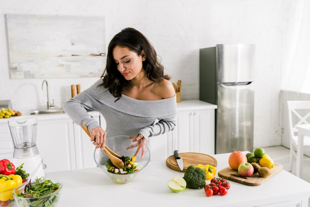mulher feliz misturando salada fresca perto de legumes em casa
  - Foto, Imagem
