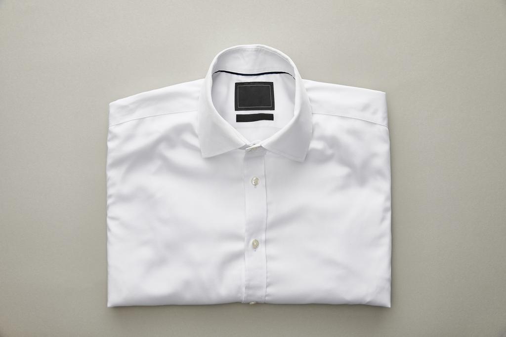 Κορυφαία όψη του απλού λευκού διπλωμένο πουκάμισο σε ανοιχτό γκρι φόντο - Φωτογραφία, εικόνα