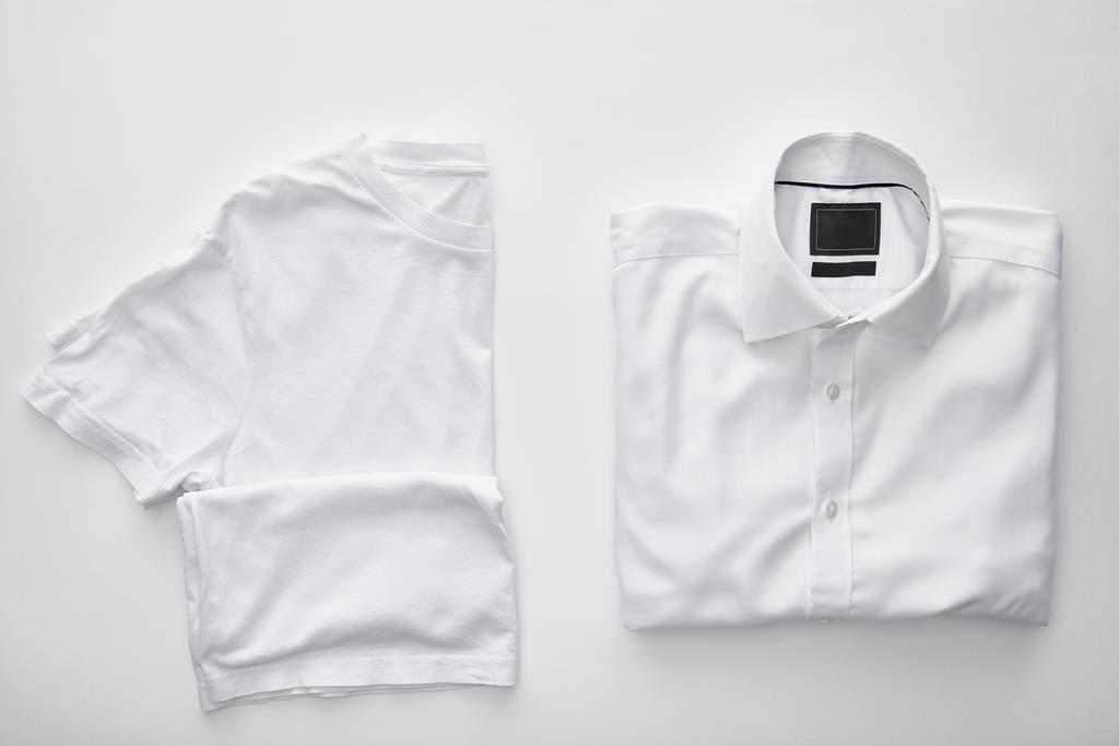 вид сверху на пустую футболку рядом с клетчатой рубашкой на белом фоне
 - Фото, изображение