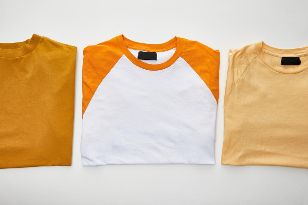 Top View van oker, beige en oranje gevouwen t-shirts op witte achtergrond - Foto, afbeelding