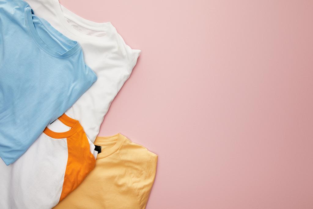 pembe arka plan üzerinde beyaz, sarı, turuncu ve mavi katlanmış t-shirt üst görünümü - Fotoğraf, Görsel