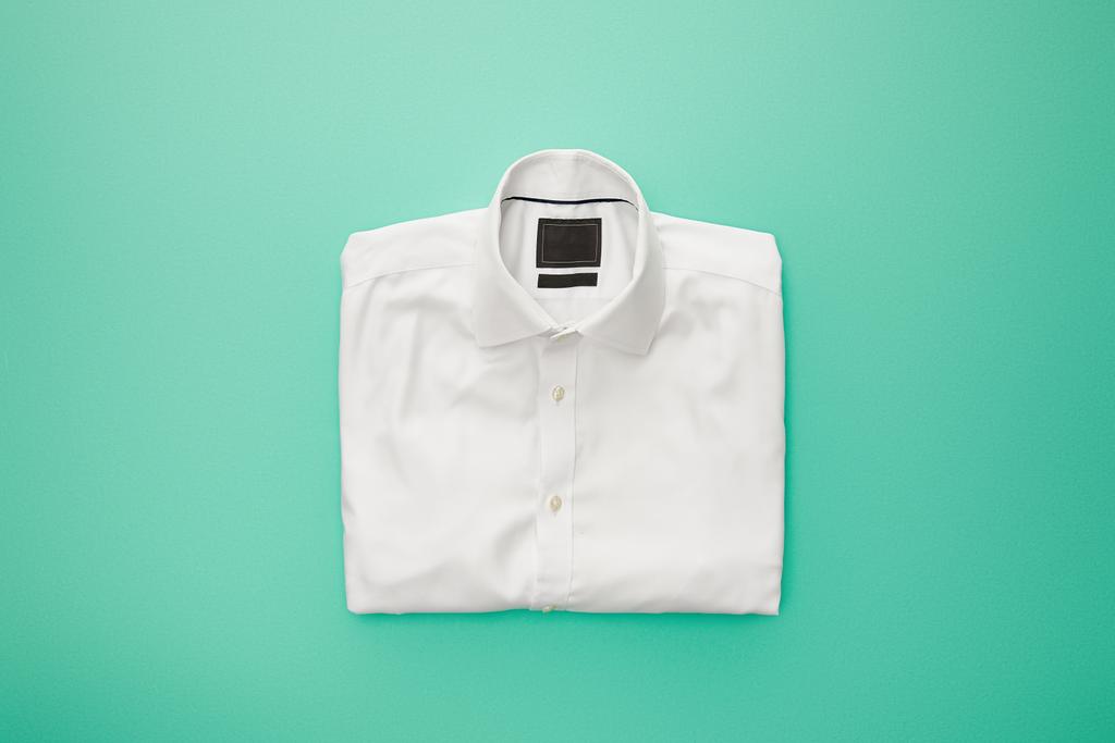 Draufsicht auf schlichtes weißes gefaltetes Hemd auf türkisfarbenem Hintergrund - Foto, Bild