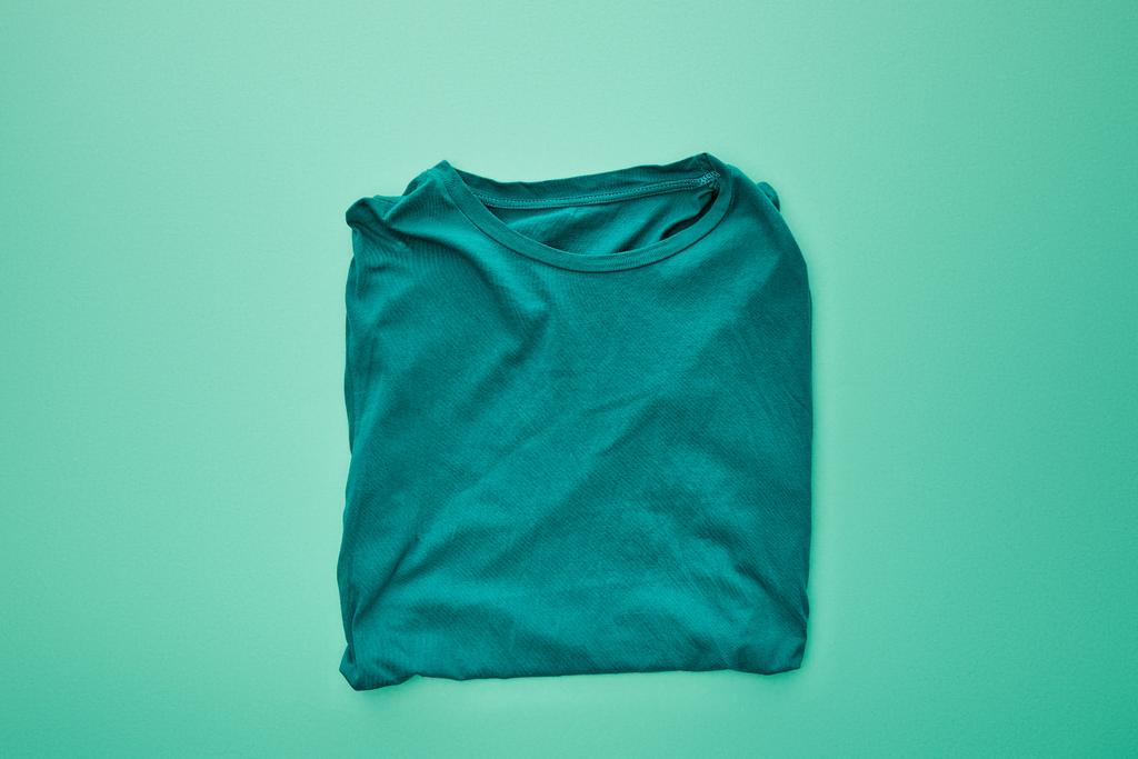 Top weergave van lege kleur gevouwen t-shirt op Turquoise achtergrond - Foto, afbeelding